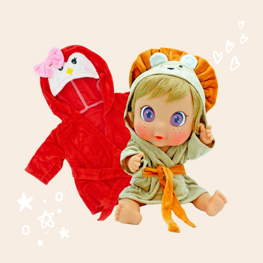Muñeco Malik de Los Nadurines con el albornoz para muñecas de león en color crema y naranja junto al albornoz de pingüino rojo con un lazo rosa.